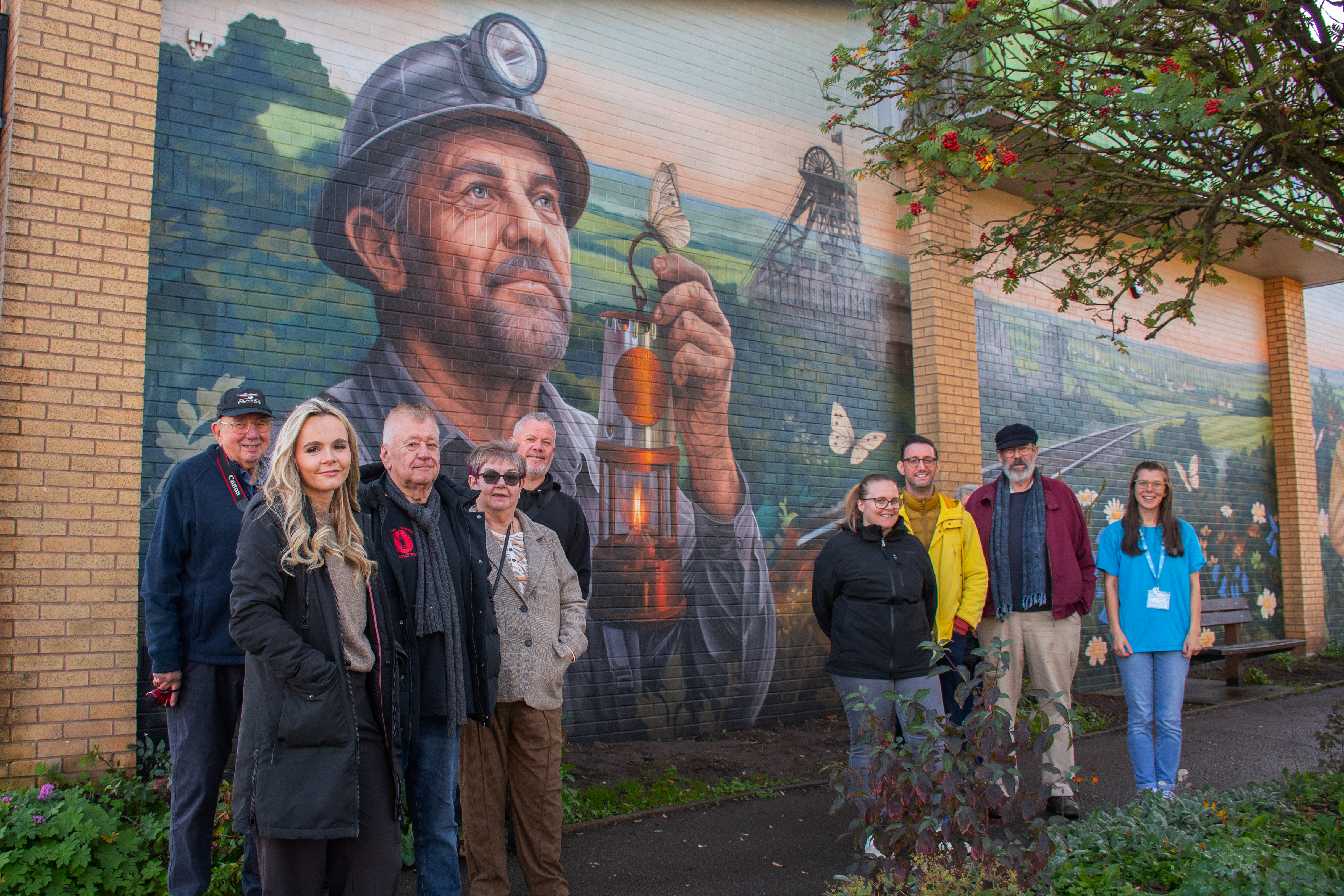 A group of people stood in front of a wall featuring a mural of a miner holding a lamp