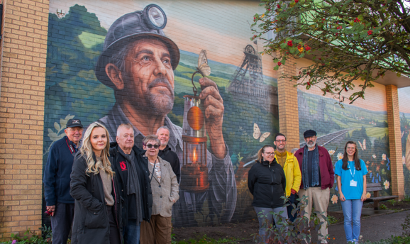 A group of people stood in front of a wall featuring a mural of a miner holding a lamp