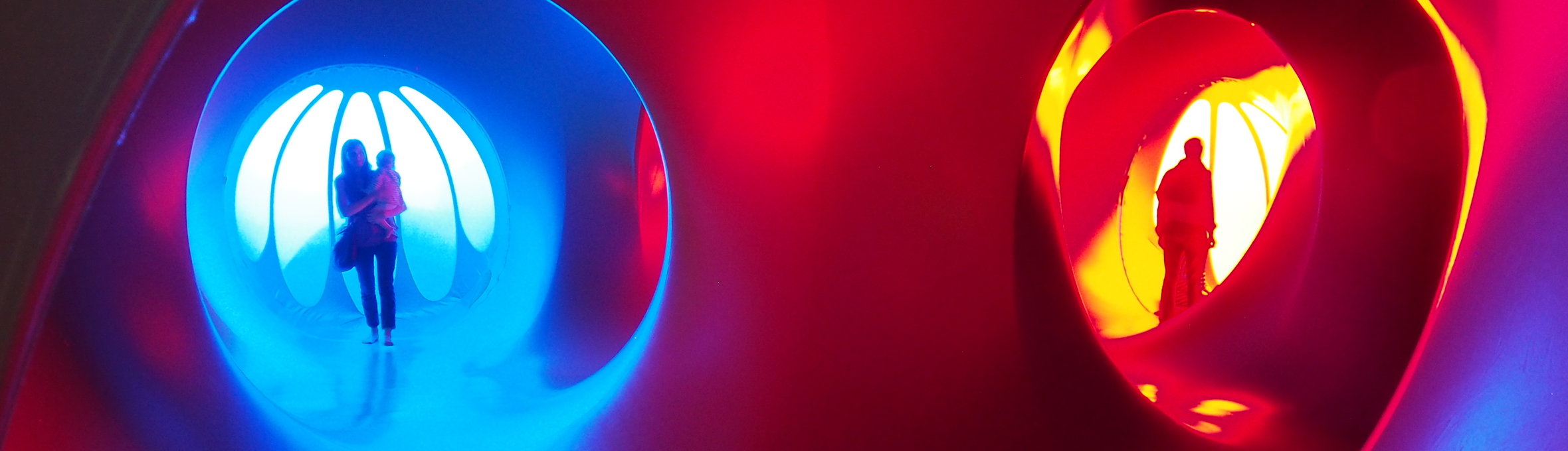 People inside a sculpture that is lit red and blue with tunnels and windows 