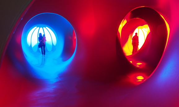 People inside a sculpture that is lit red and blue with tunnels and windows 