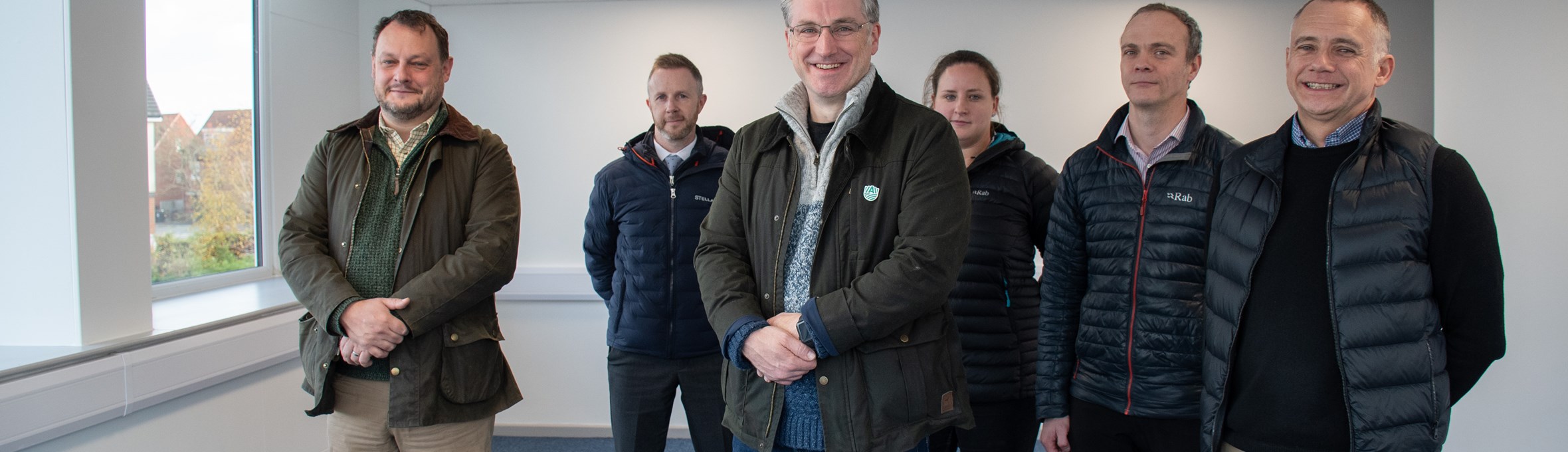 Five men and a woman stand in an office unit smiling at the camera 