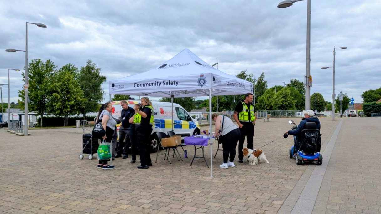 Men and women in high vis vests talk to residents under a white gazebo