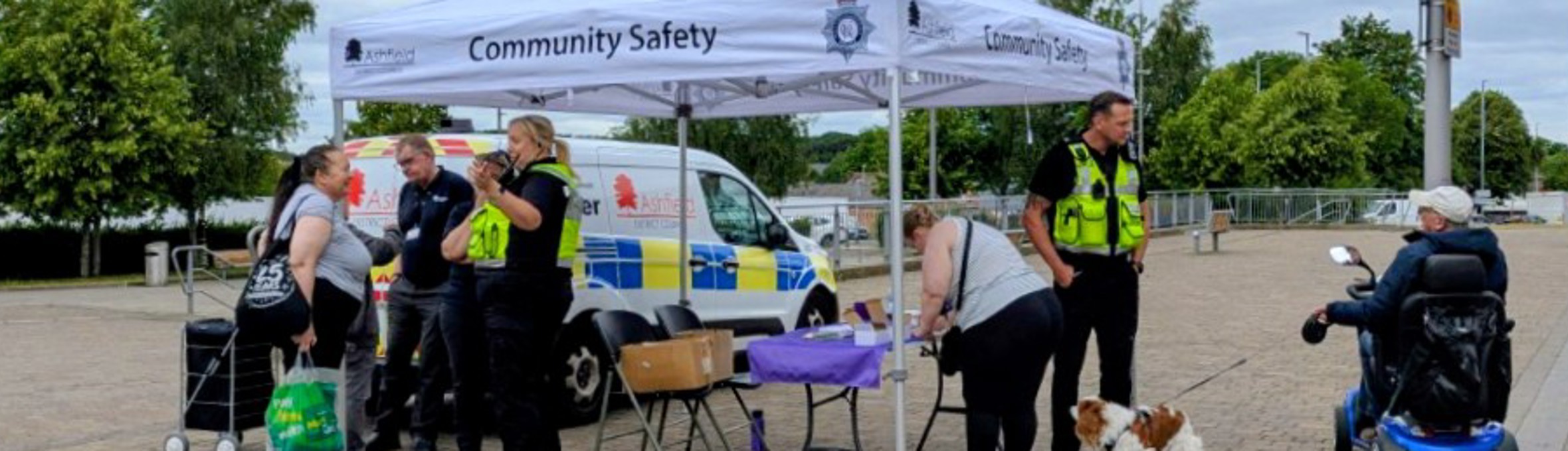 Men and women in high vis vests talk to residents under a white gazebo