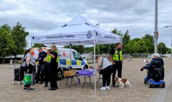 Men and women in high vis vests talk to residents under a white gazebo