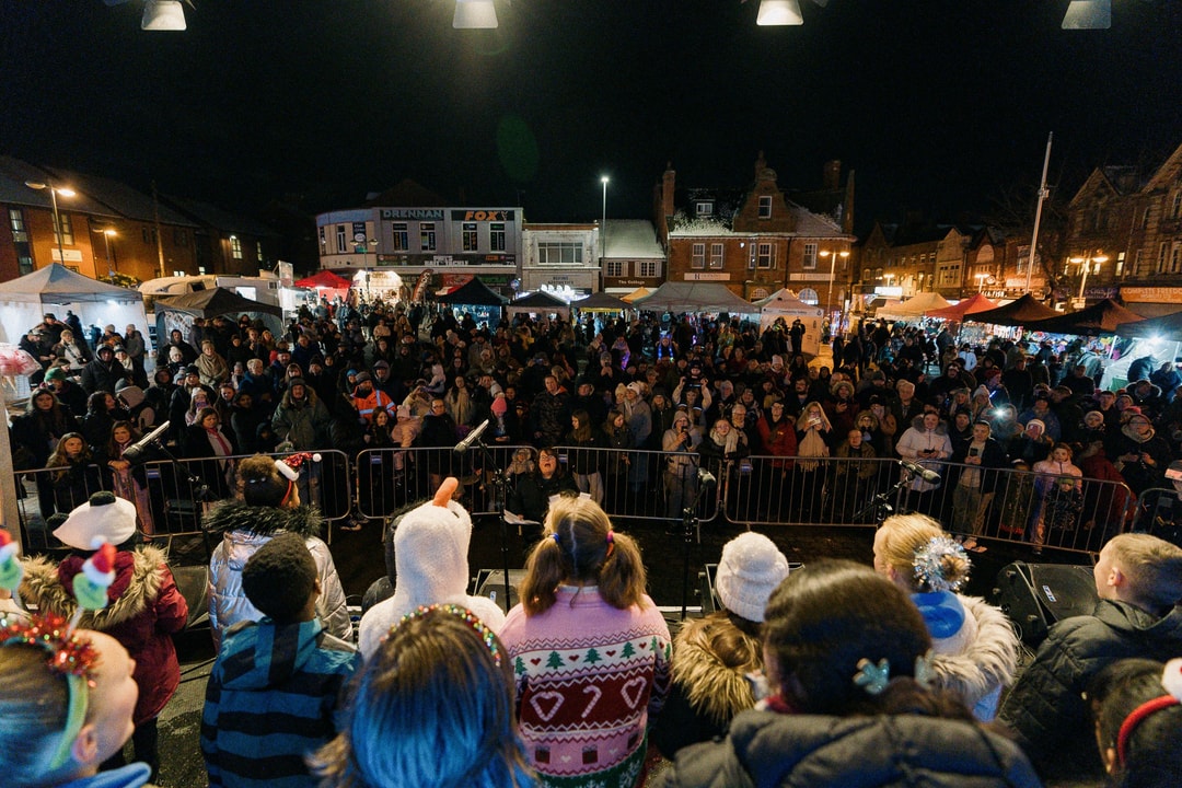Children on stage look over a crowd of people in Sutton with a market behind them