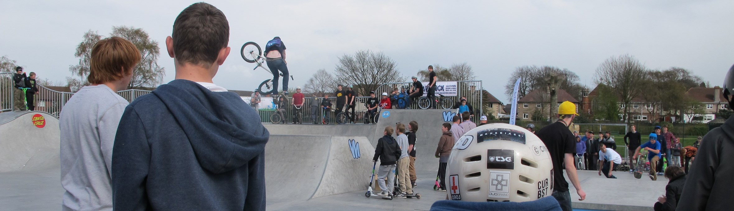 Young people with backs to camera watching others do bike and skate tricks on ramps