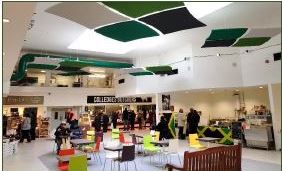 View of chairs and tables under a glass atrium, market stalls in background with people shopping