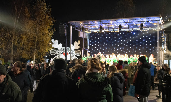 People watch a stage with a backdrop of fairy lights with a light up reindeer to the left