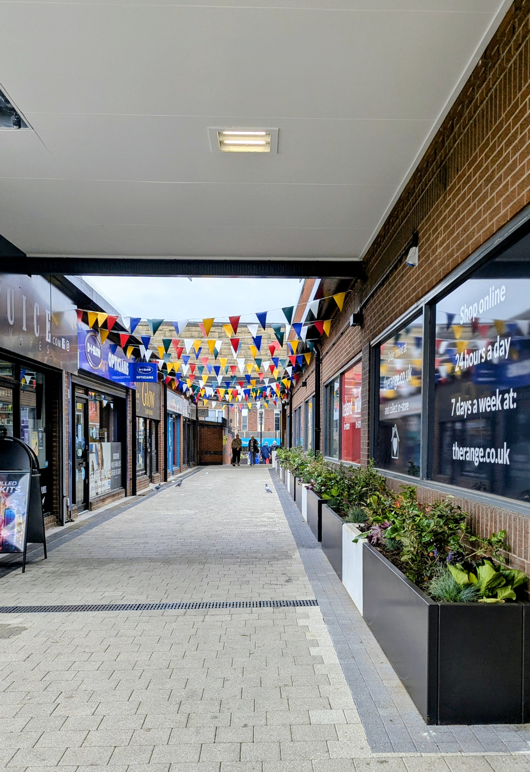 A pedestrian walkway with coloured bunting hanging between buildings 