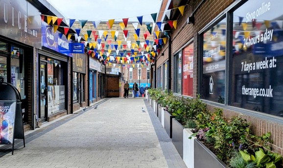 A pedestrian walkway with coloured bunting hanging between buildings 