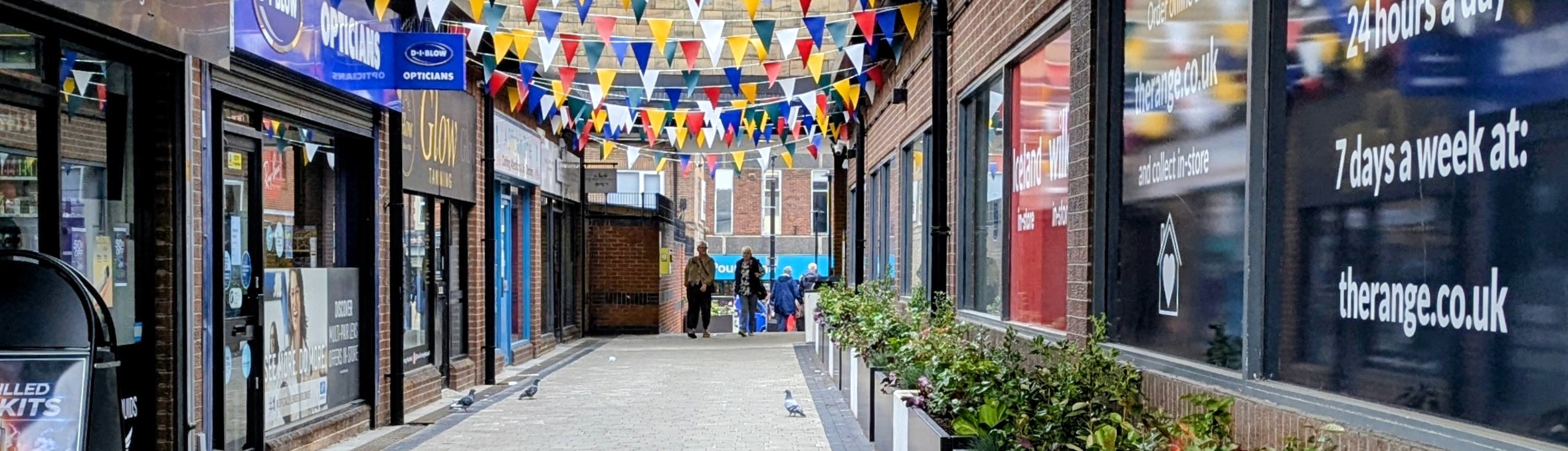 A pedestrian walkway with coloured bunting hanging between buildings 