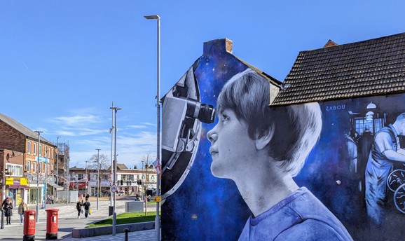 A photo-realistic mural on the side of a building shows a young girl looking through a telescope