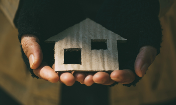 A pair of hands in fingerless gloves, holding a small cardboard cutout of a house