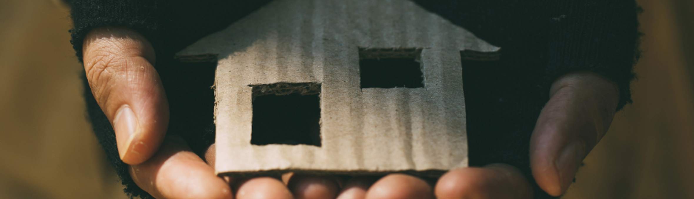 A pair of hands in fingerless gloves, holding a small cardboard cutout of a house