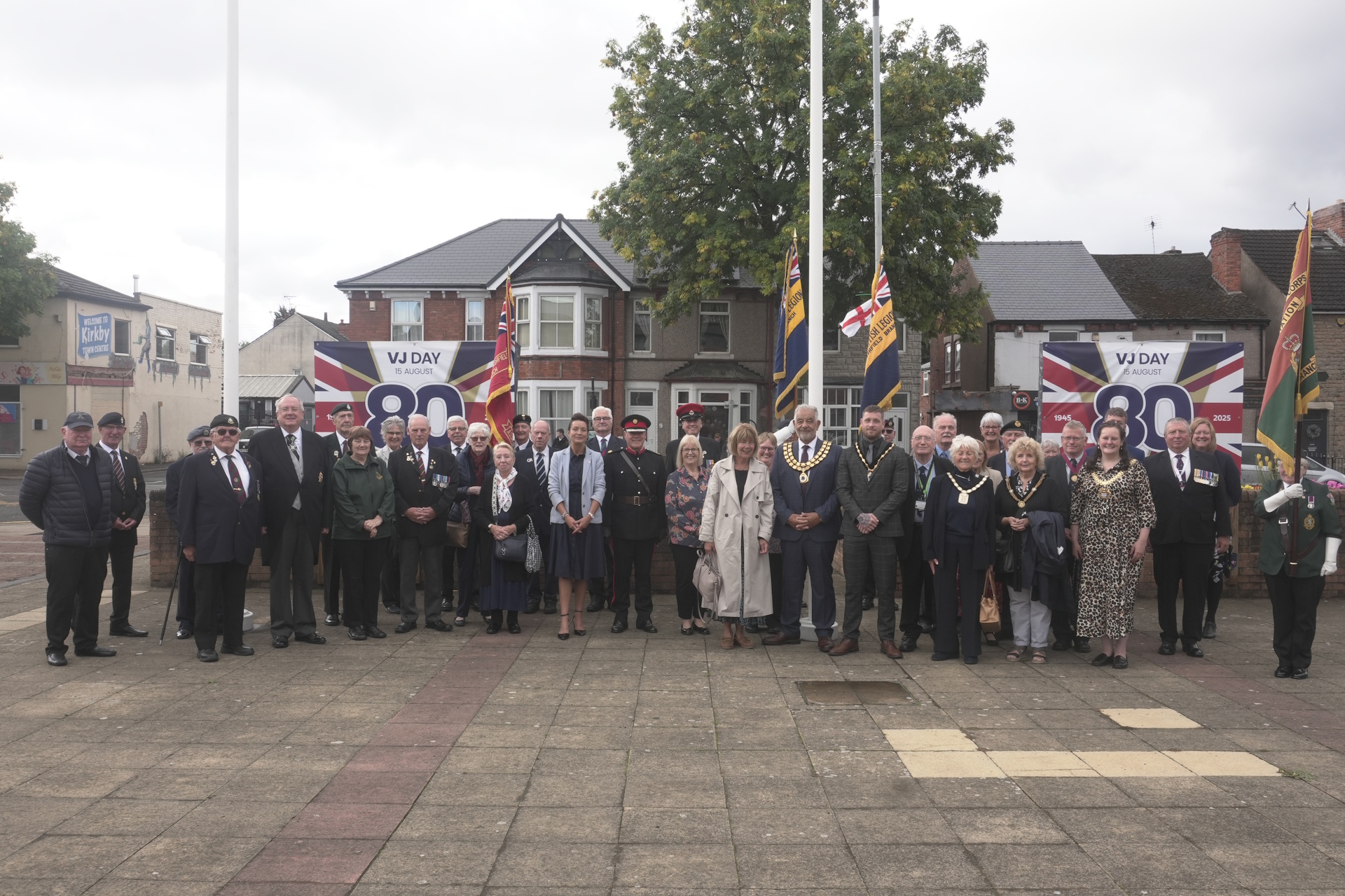 A crowd of officials and local notables beside the flags raised for Merchant Navy Day outside ADC