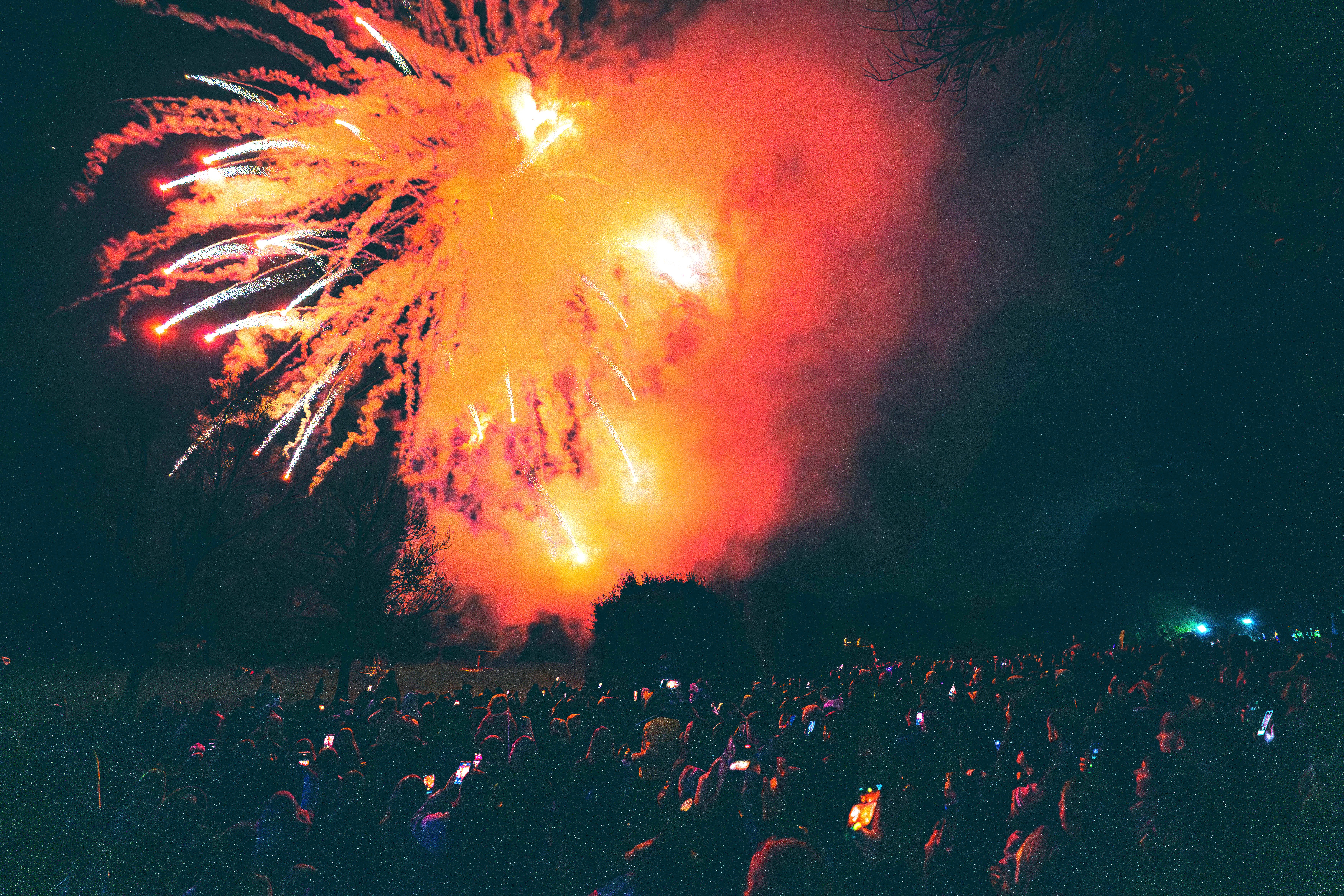 A crowd of people watching a firework display with an orange firework illuminating the crowds
