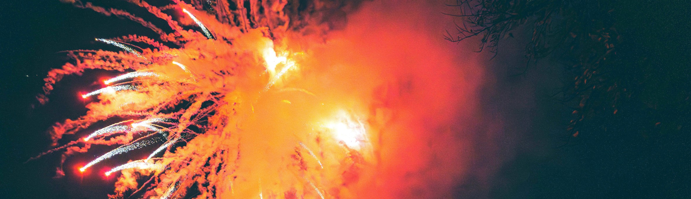 A crowd of people watching a firework display with an orange firework illuminating the crowds