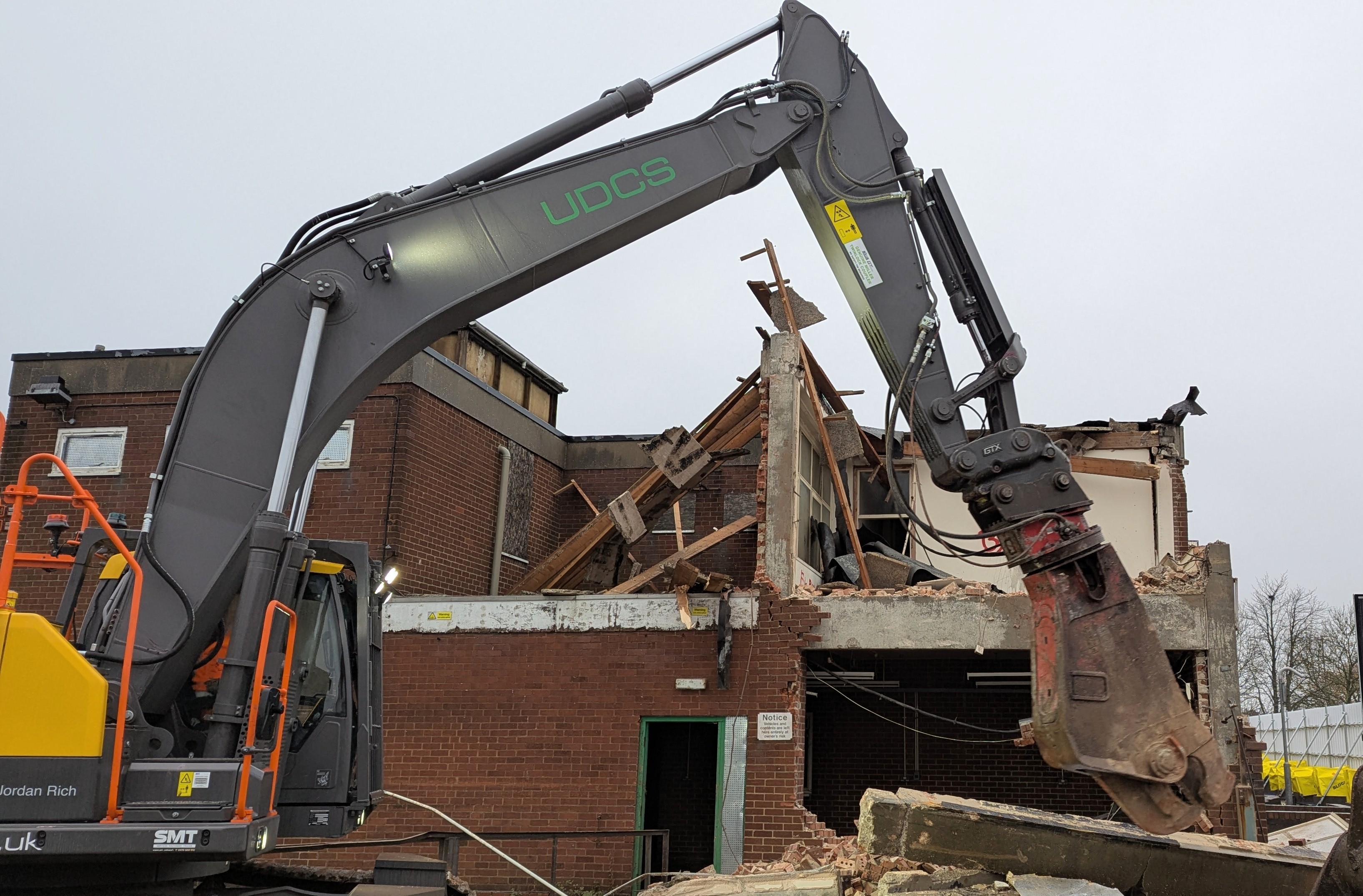 A red brick building in a state of partial demolition with a machine in front of the building