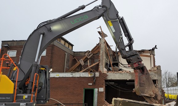 A red brick building in a state of partial demolition with a machine in front of the building
