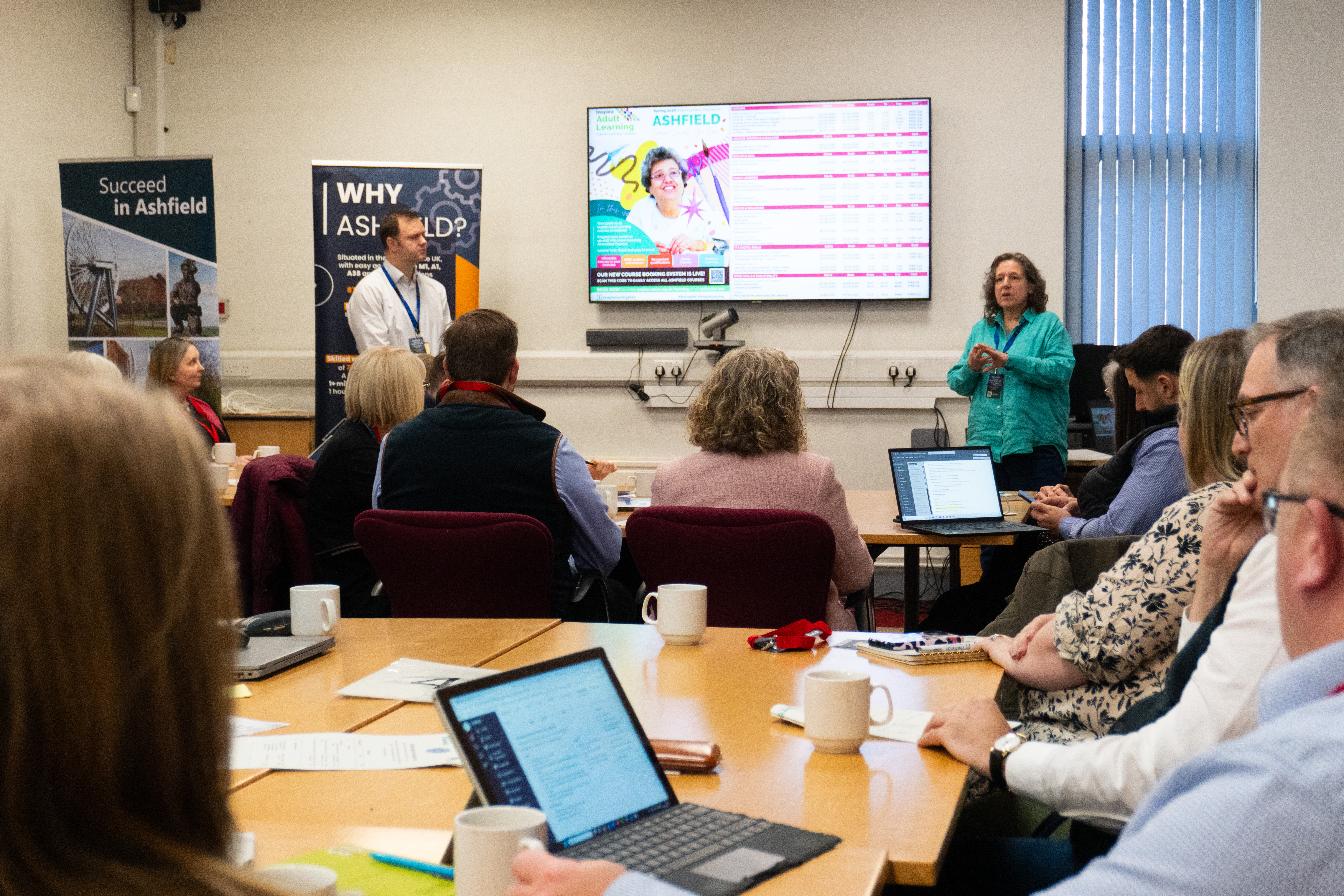 People in a meeting looking at laptops and a big screen 