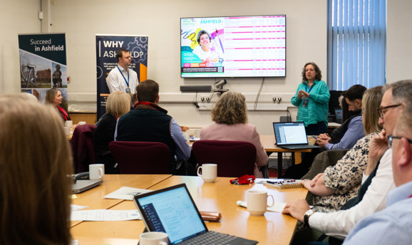 People in a meeting looking at laptops and a big screen 
