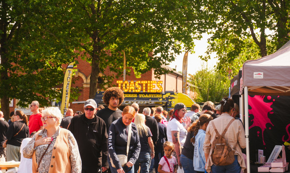 a crowd of people stood in front of various food stalls 