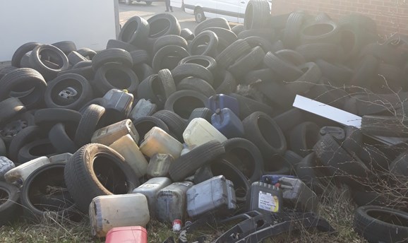 Example of fly tipping - tyres and plastic containers in a heap next to a building