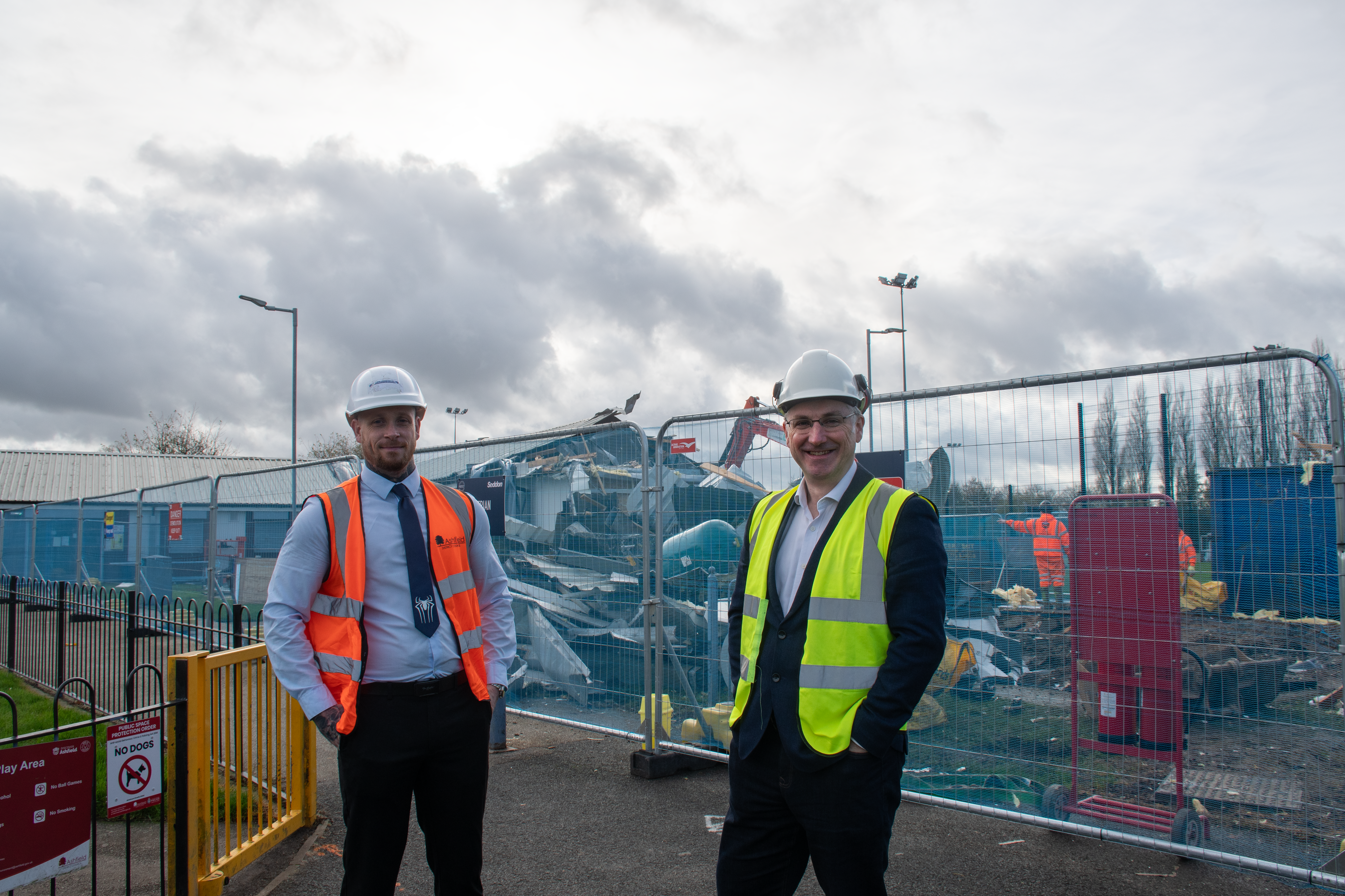 Two men in high vis stand in front of a half demolished changing room on Kingsway Park