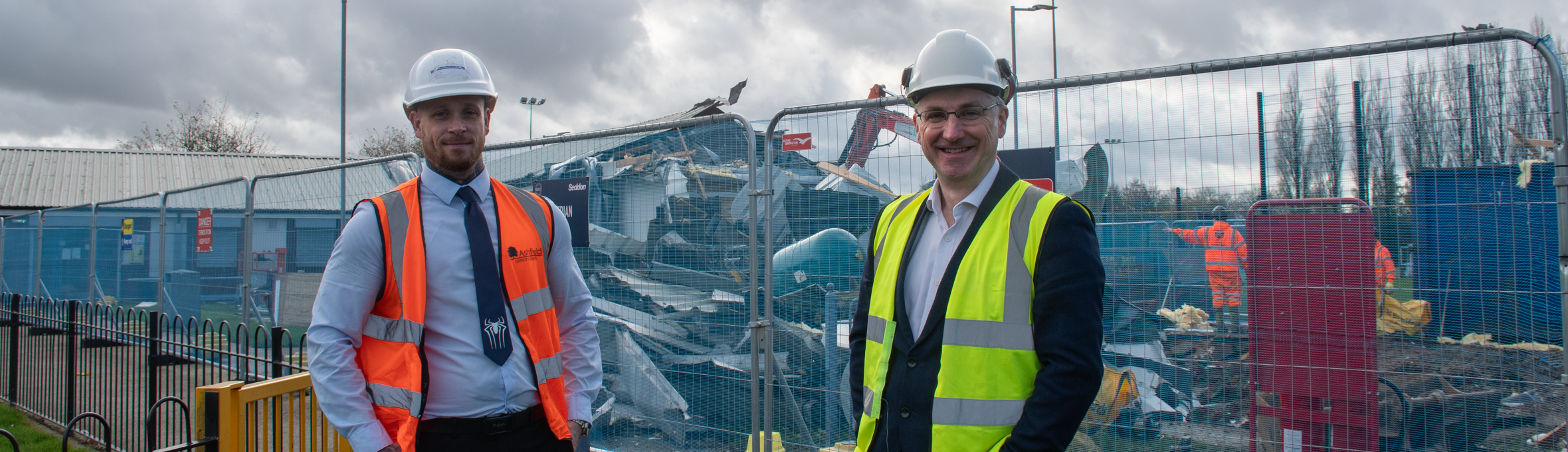 Two men in high vis stand in front of a half demolished changing room on Kingsway Park
