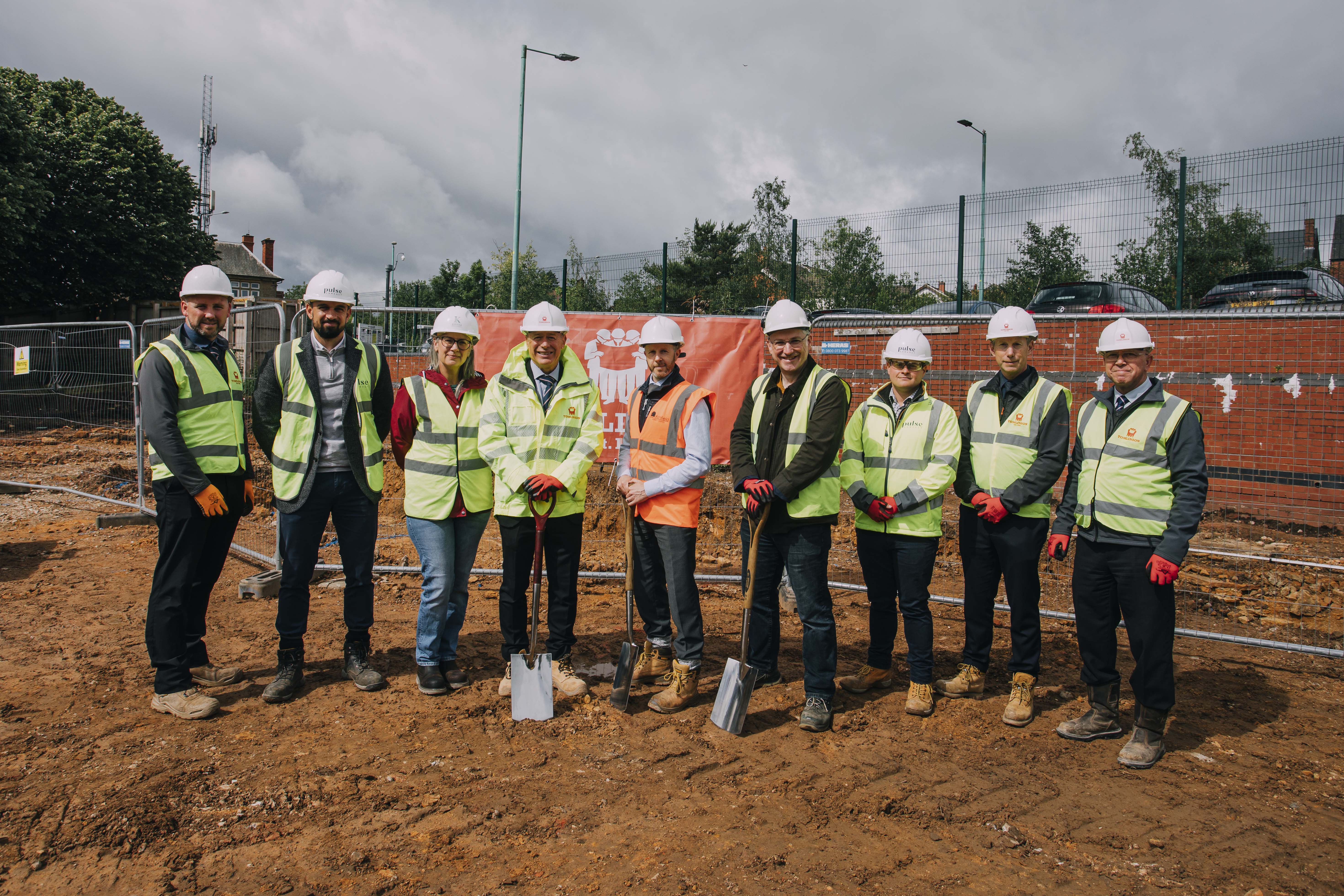 A group of men and one woman in high vis vests look at the camera, they are stood on mud 