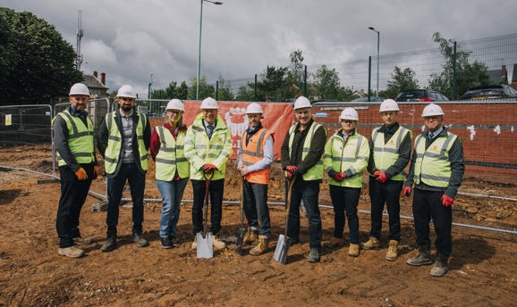 A group of men and one woman in high vis vests look at the camera, they are stood on mud 