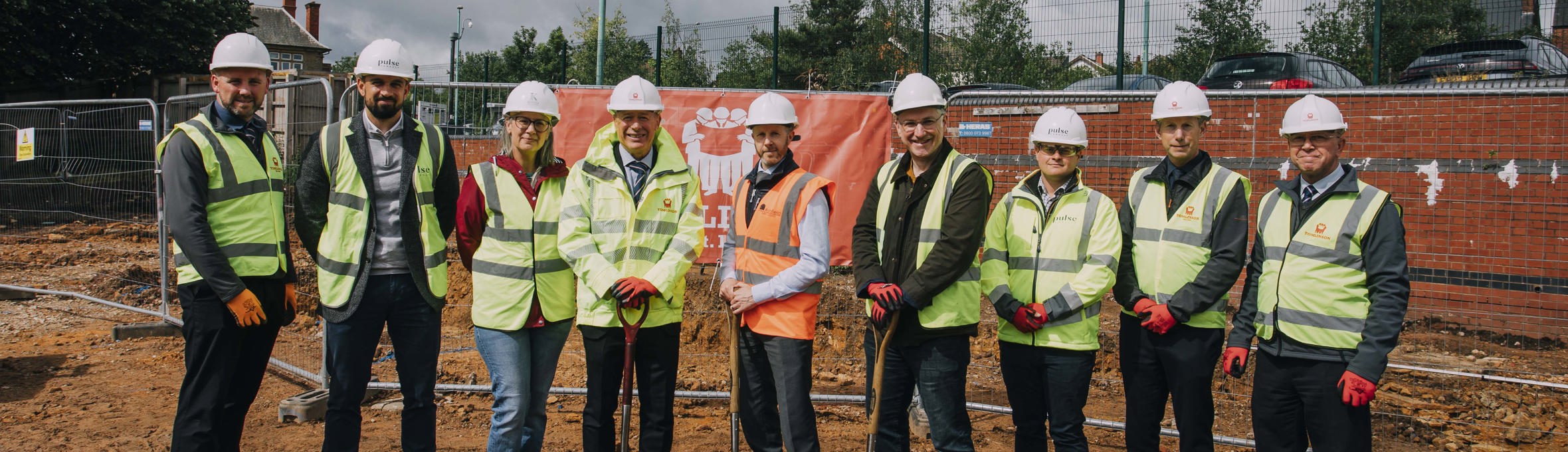 A group of men and one woman in high vis vests look at the camera, they are stood on mud 
