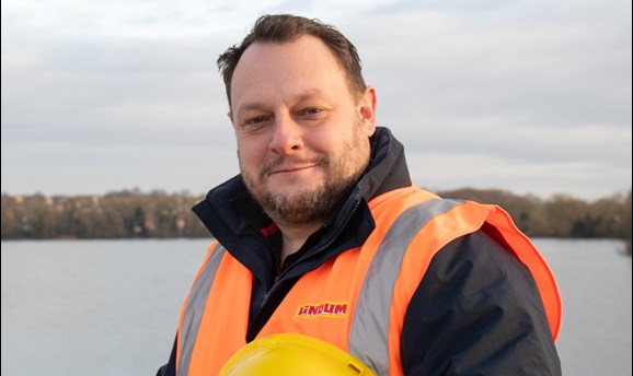 Cllr Jason Zadrozny smiles at the camera, he is holding a hard hat and wearing a high vis vest