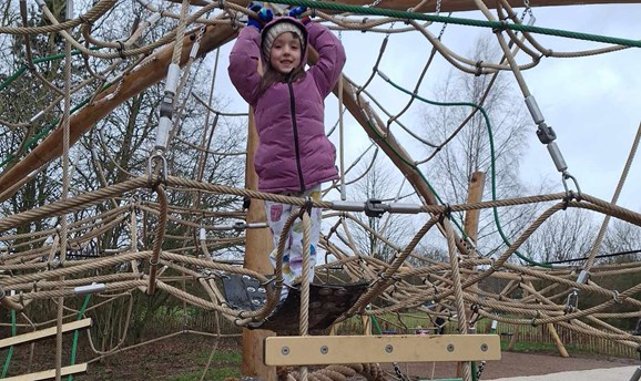 A young girl is clinging onto the climbing tree in a purple coat 