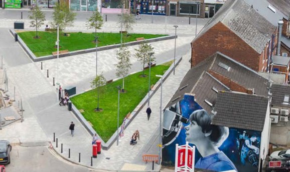 Image of houses and shops with seating in the middle and grass areas each side of the seating