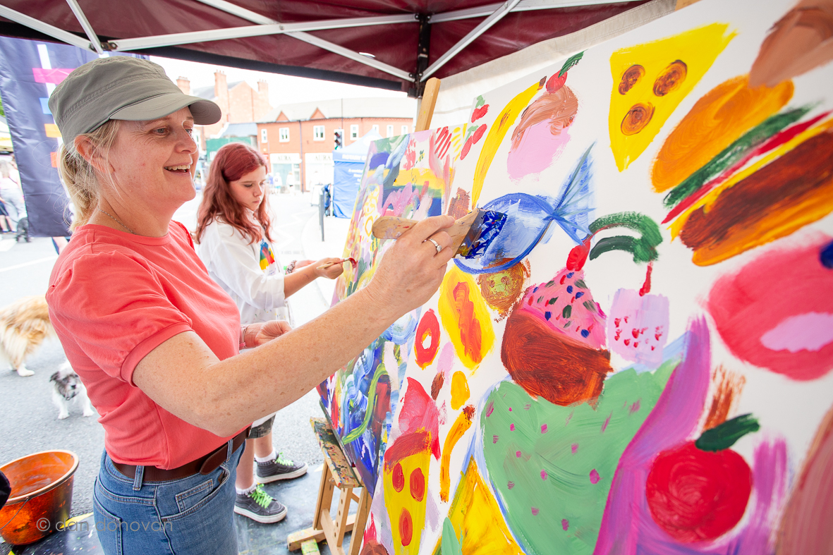 a woman is smiling whilst she paints a blue fish on a canvas 