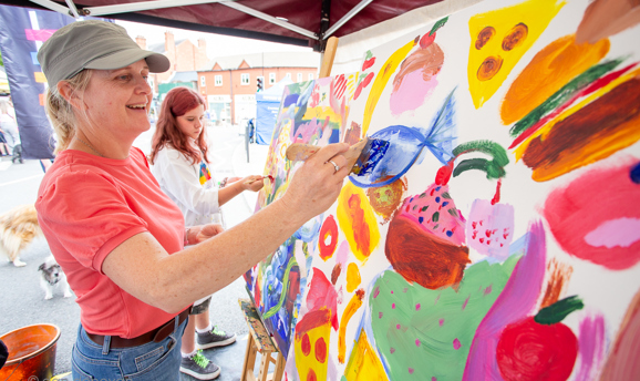 a woman is smiling whilst she paints a blue fish on a canvas 