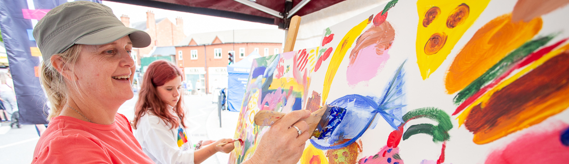 a woman is smiling whilst she paints a blue fish on a canvas 