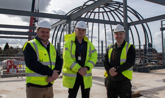 Three men smile at the camera, they are stood in front of a dome made of steel 